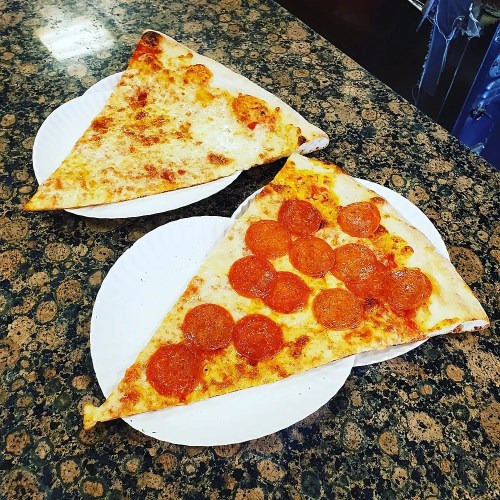 Two large slices of pizza on white plates: one plain cheese and one topped with pepperoni, on a speckled countertop.
