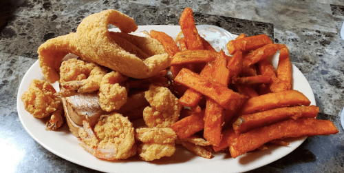 A plate of fried shrimp, a fish fillet, and sweet potato fries, served with a dipping sauce.