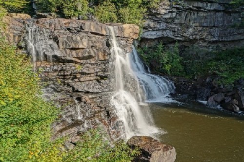 A scenic waterfall cascading over rocky cliffs into a calm pool, surrounded by lush greenery.
