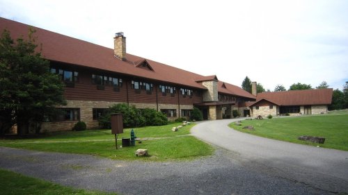 A large, rustic building with a brown roof and stone accents, surrounded by green grass and trees.