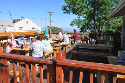 A sunny outdoor dining area with wooden tables and people enjoying their meals on a deck.