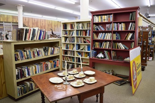 A cozy bookstore interior featuring two bookshelves filled with books and a table set with plates and candles.