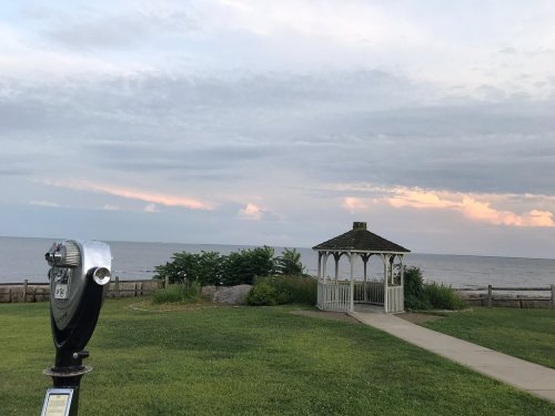 A scenic view of a gazebo by the water, with a coin-operated viewer in the foreground and cloudy skies above.