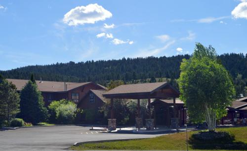 A scenic view of a lodge entrance surrounded by trees and mountains under a clear blue sky with fluffy clouds.