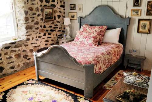 Cozy bedroom featuring a floral bedspread, stone walls, wooden floor, and vintage decor.