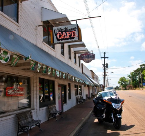 Exterior of White House Café with a motorcycle parked outside, featuring a row of benches and decorative banners.