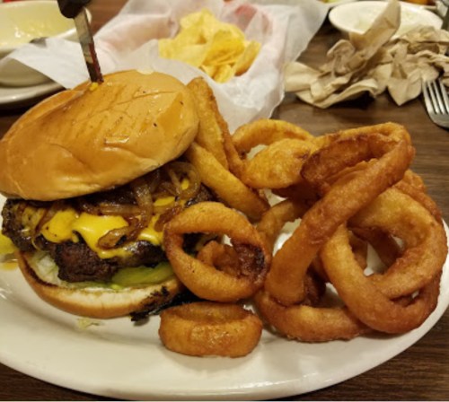 A juicy cheeseburger with onions and pickles, served with crispy onion rings on a plate.