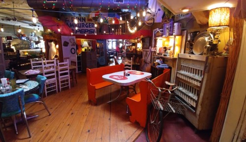 A cozy, eclectic restaurant interior with colorful seating, string lights, and vintage decor.