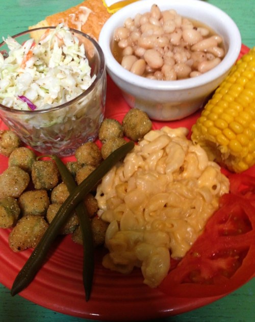 A colorful plate featuring macaroni and cheese, corn on the cob, coleslaw, white beans, and fried okra.