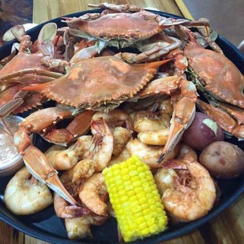 A platter of seafood featuring crabs, shrimp, corn, and potatoes, served with a dipping sauce.