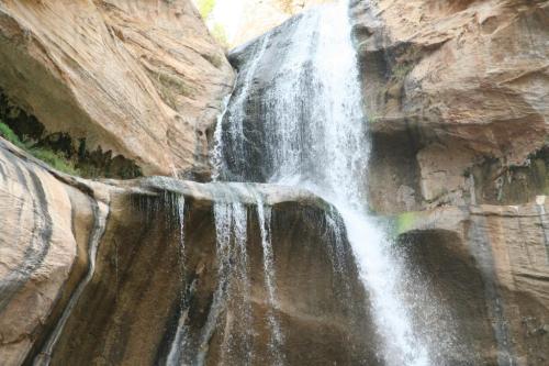 A cascading waterfall flows down rocky cliffs, surrounded by natural stone formations and greenery.