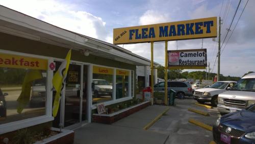 Exterior of Oak Hill Flea Market with a sign, featuring a restaurant and parked cars. Bright sky in the background.