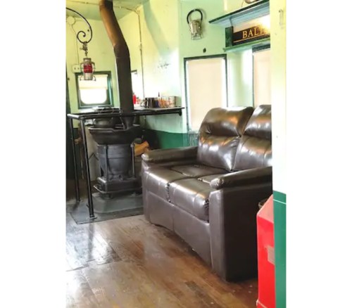 A cozy interior featuring a brown leather couch, a small table, and a wood stove in a green and white room.