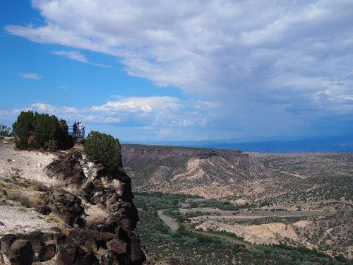 A scenic view from a rocky cliff overlooking a river and expansive landscape under a partly cloudy sky.