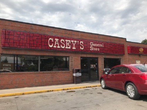 Exterior of Casey's General Store with a red sign, large windows, and a parked red car in front.