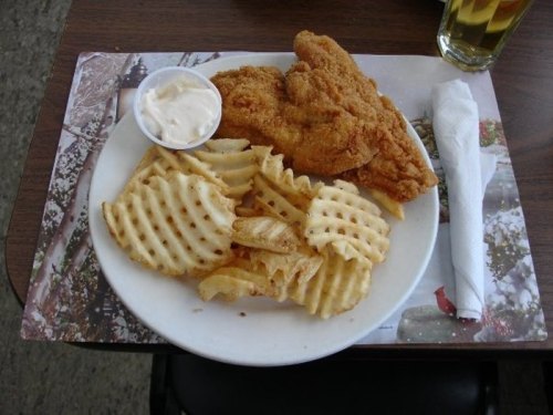 A plate with two pieces of fried chicken, waffle fries, and a small cup of dipping sauce on a wooden table.