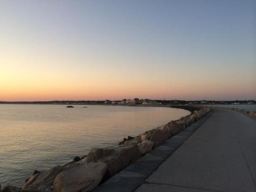 A serene waterfront view at sunset, featuring a rocky path along calm waters and distant buildings.