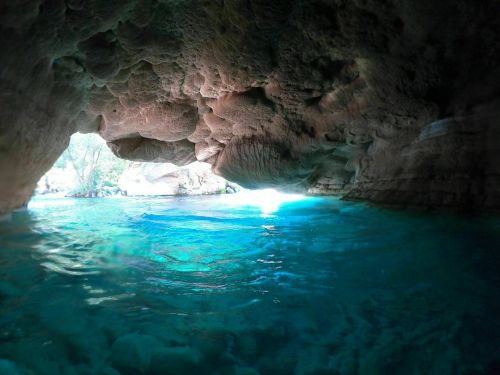 A serene cave entrance with turquoise water and sunlight streaming in, creating a tranquil atmosphere.