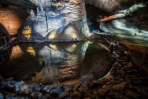 A dimly lit cave with a still water pool reflecting the rocky walls and illuminated features.