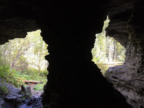 View from inside a cave, showing two openings framed by rocky walls and greenery outside.