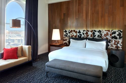 Modern hotel room featuring a king bed, stylish seating, and large windows with a view. Warm wood accents and contemporary decor.