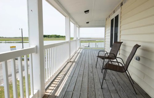 A spacious porch with two chairs overlooking a calm water view and green landscape in the background.