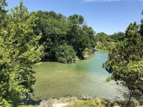 A serene river surrounded by lush green trees under a clear blue sky.