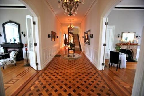 Elegant hallway with a patterned wooden floor, leading to a staircase and adorned with chandeliers and artwork.