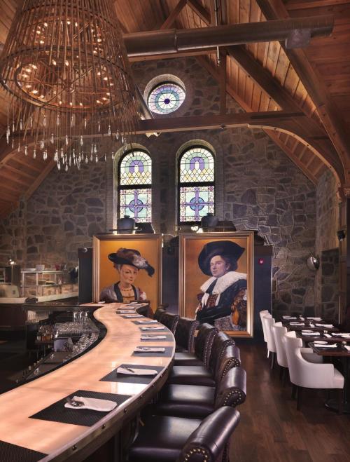 A stylish restaurant interior with a curved bar, large portraits, stained glass windows, and wooden beams.
