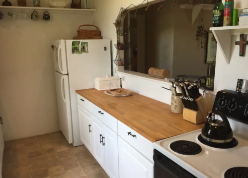A cozy kitchen with white cabinets, a wooden countertop, a stove, and a refrigerator, featuring kitchen utensils and decor.