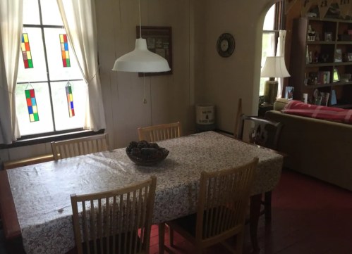 A cozy dining area with a table, wooden chairs, and colorful stained glass windows, featuring a warm, inviting atmosphere.