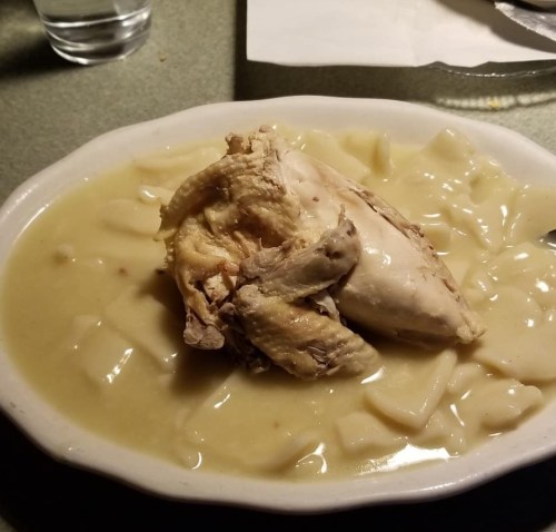 A bowl of chicken and dumplings featuring a piece of chicken in creamy broth with soft dumplings.