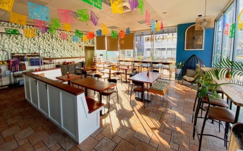 Brightly lit restaurant interior with colorful papel picado decorations, wooden tables, and a cozy seating area.