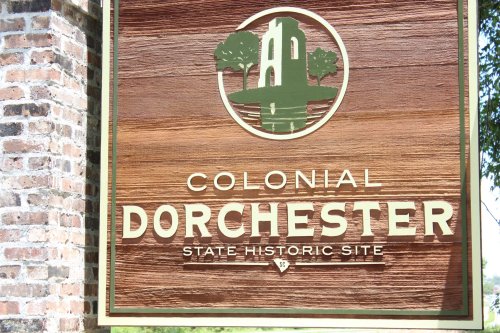 Sign for Colonial Dorchester State Historic Site, featuring a wooden background and a circular emblem with trees.