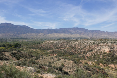 A panoramic view of rolling hills and mountains under a clear blue sky, showcasing a desert landscape.