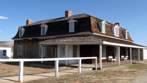 Historic two-story house with a sloped roof, wooden siding, and a porch, set against a clear blue sky.