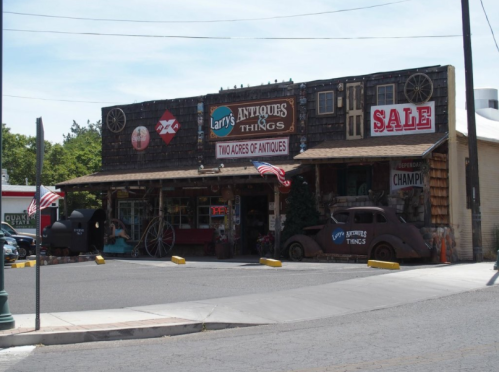 A rustic antique shop with a wooden facade, vintage signs, and American flags outside, promoting a sale.