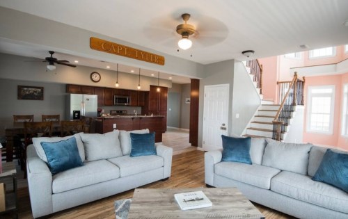 Modern living room with two sofas, a dining area, and a staircase, featuring a sign that reads "CAPT. TYLER."