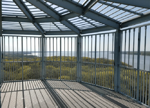 View from a metal observation deck overlooking a river and lush green landscape under a clear blue sky.