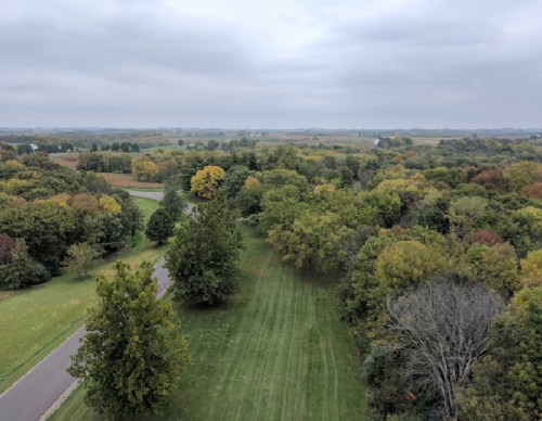 Aerial view of a lush green landscape with trees and a winding road under a cloudy sky.