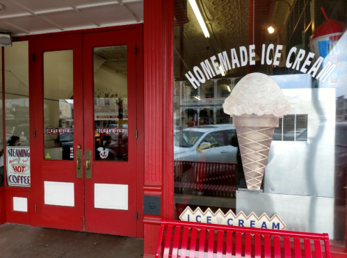 Red double doors lead to an ice cream shop, featuring a large window display of a cone with a scoop of ice cream.