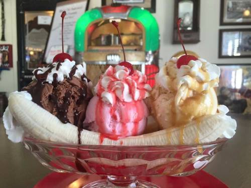 A banana split with three scoops of ice cream—chocolate, strawberry, and vanilla—topped with whipped cream and cherries.