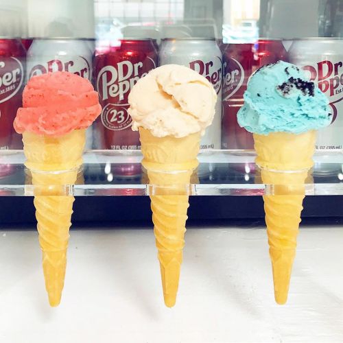 Three ice cream cones in a row: pink, white, and blue, with Dr Pepper cans in the background.