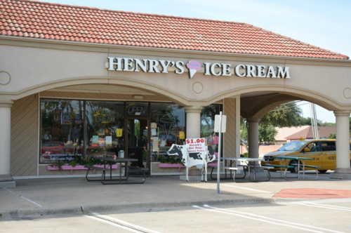 Exterior of Henry's Ice Cream shop with a red-tiled roof, open sign, and a cow sign advertising $1 ice cream.