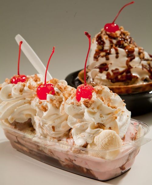 A dessert dish with three scoops of ice cream topped with whipped cream, crushed nuts, and cherries, alongside a chocolate sundae.