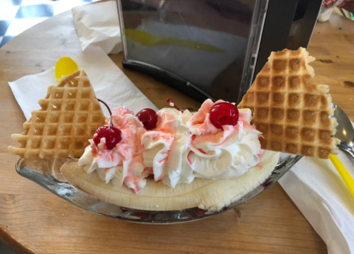 A banana split topped with whipped cream, cherries, and two waffle cones on a wooden table.