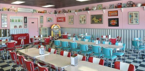 A retro diner with pink walls, red and blue chairs, and a jukebox, featuring vintage decor and a cozy atmosphere.