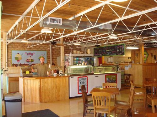 A cozy restaurant interior with wooden decor, a counter, and a smiling staff member welcoming customers.