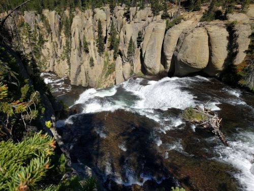 A scenic view of a waterfall cascading over rocky cliffs, surrounded by lush greenery and a flowing river below.