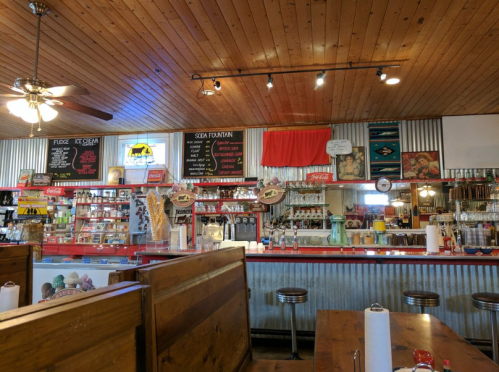 A vintage soda fountain shop with wooden decor, a long counter, and colorful menu boards on the walls.